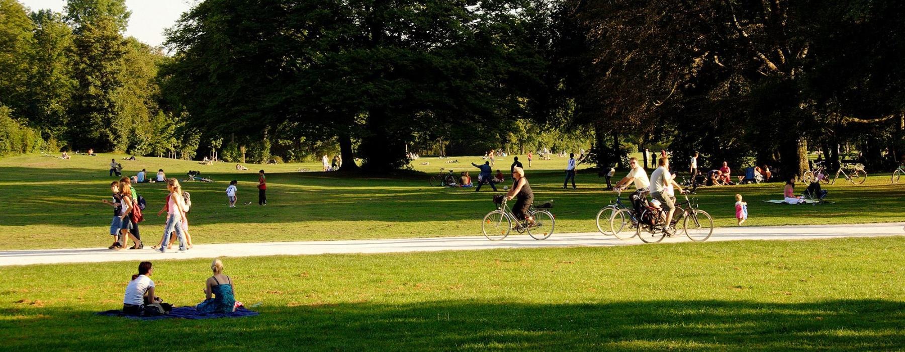 A park with many people riding bikes, having a picnic, and walking.