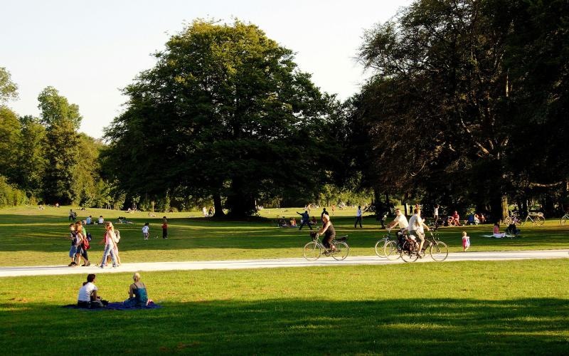 A park with many people riding bikes, having a picnic, and walking.