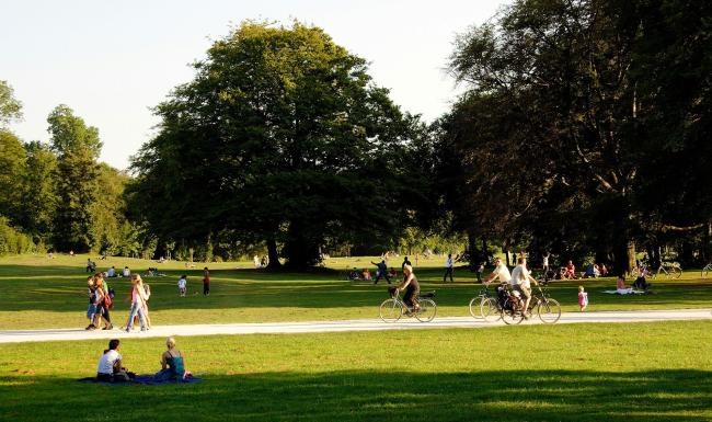 A park with many people riding bikes, having a picnic, and walking.